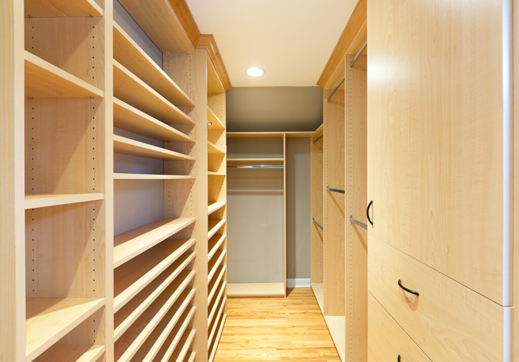 A walk-in closet featuring full height clothes hanging storage, shoes shelves, storage shelves and drawers, hardwood floor and crown molding.
