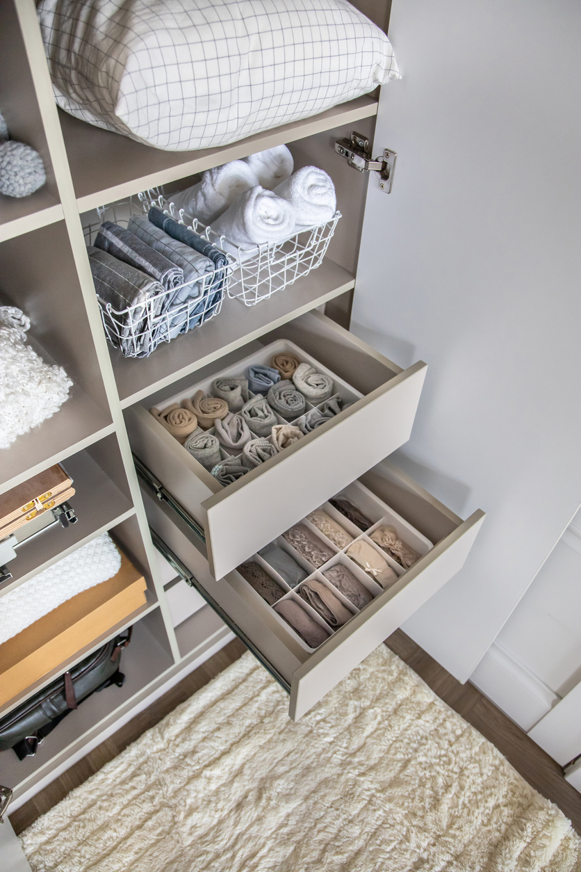 A built-in closet organizer with shelves, drawers, and baskets holding pillows and rolled sheets and pillow cases.