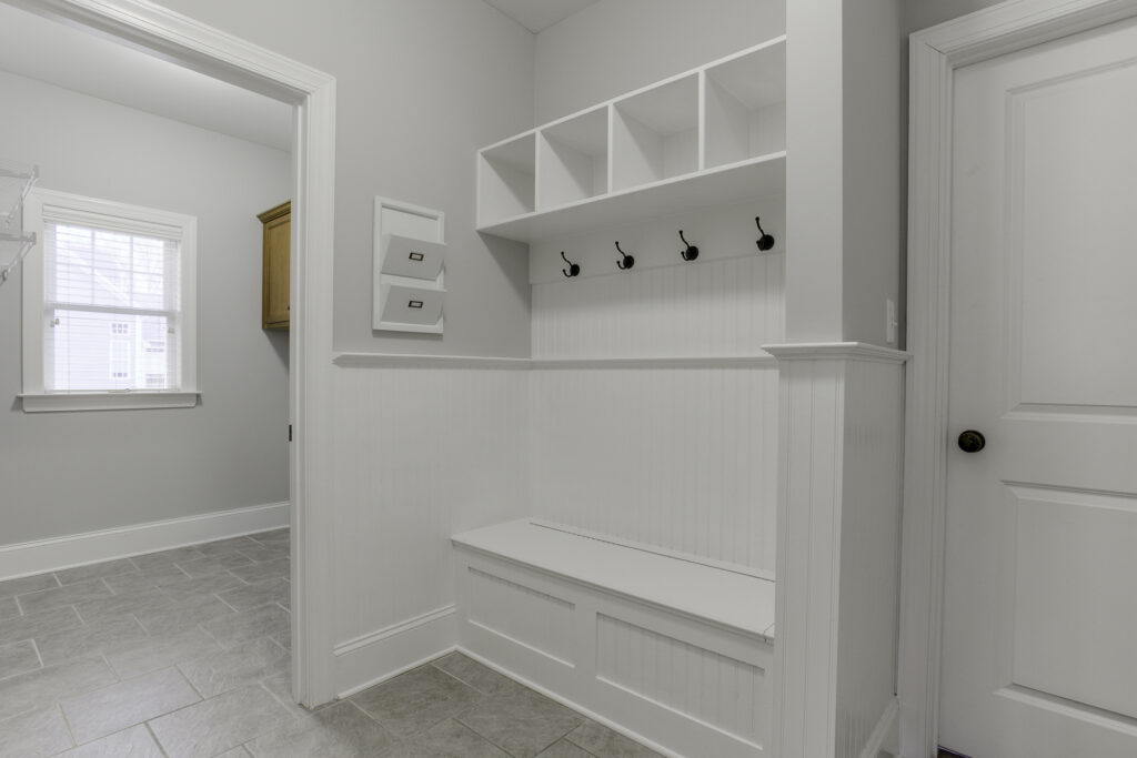 Spacious mudroom featuring a bench with hooks and storage compartments, with an adjacent laundry space. This design emphasizes organization and convenience, creating a welcoming and practical entrance while offering ample storage solutions for a busy household.