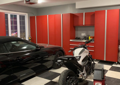A garage features red cabinets, a black car, and a motorcycle on a checkered floor with tools and equipment around.